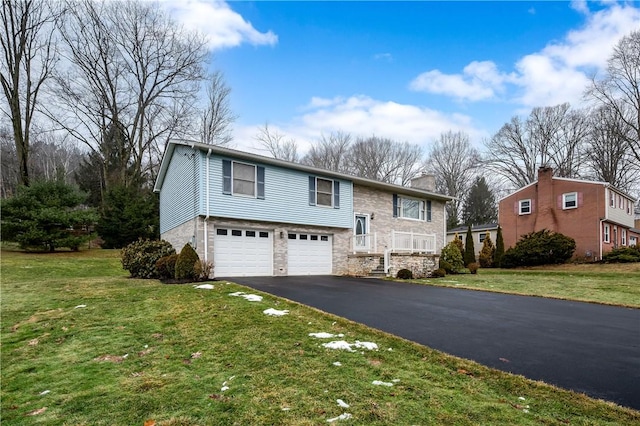 raised ranch featuring an attached garage, a chimney, aphalt driveway, and a front yard