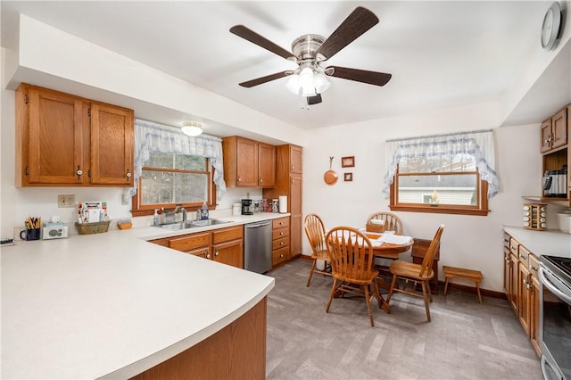 kitchen with ceiling fan, stainless steel appliances, a sink, light countertops, and brown cabinetry