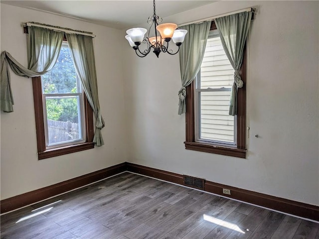 unfurnished dining area featuring visible vents, baseboards, a chandelier, and wood finished floors