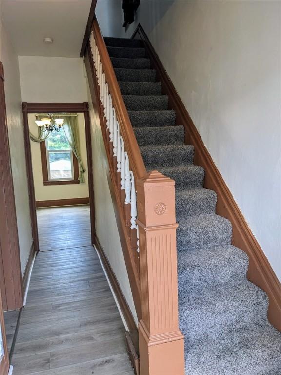 stairs featuring an inviting chandelier, baseboards, and wood finished floors