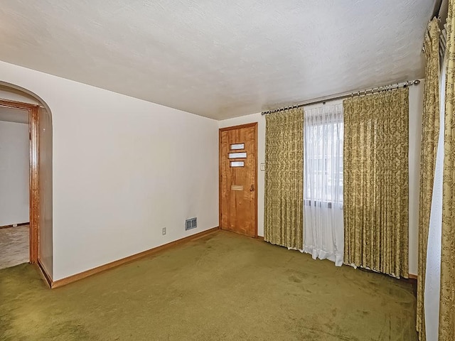 unfurnished room with arched walkways, carpet, visible vents, a textured ceiling, and baseboards