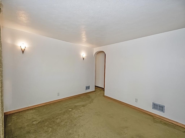 spare room featuring arched walkways, a textured ceiling, carpet floors, visible vents, and baseboards