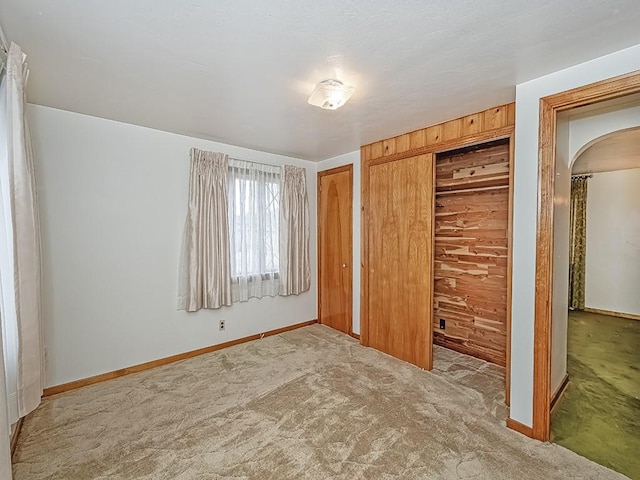 unfurnished bedroom with arched walkways, carpet, and baseboards