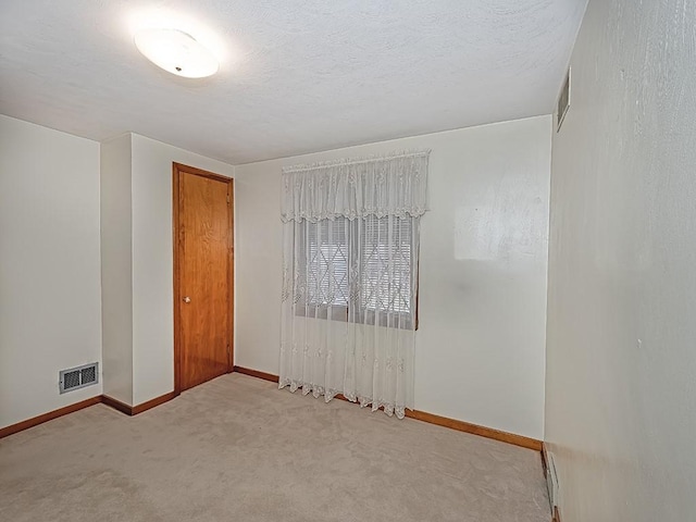 carpeted empty room with a textured ceiling, visible vents, and baseboards