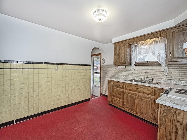 kitchen with arched walkways, a wainscoted wall, light countertops, dark colored carpet, and a sink