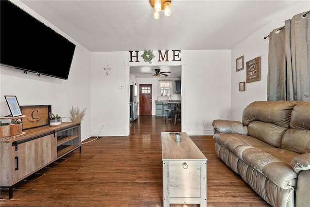 living area featuring dark wood-type flooring, a ceiling fan, and baseboards