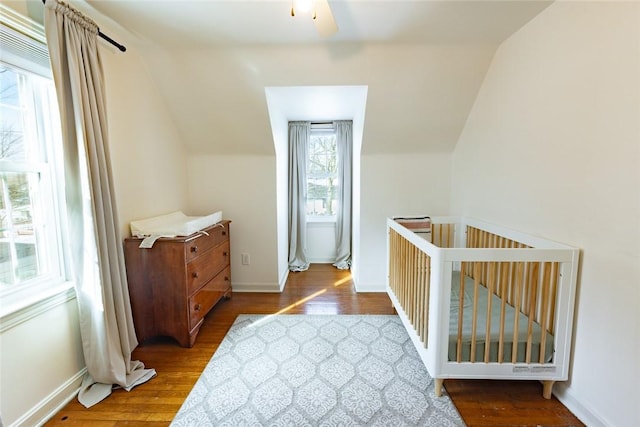 bedroom featuring lofted ceiling, a nursery area, wood finished floors, and baseboards