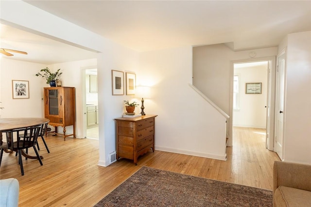 hall with baseboards, visible vents, and light wood finished floors