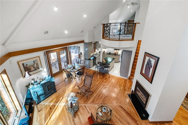 living area featuring high vaulted ceiling, a glass covered fireplace, wood finished floors, and french doors