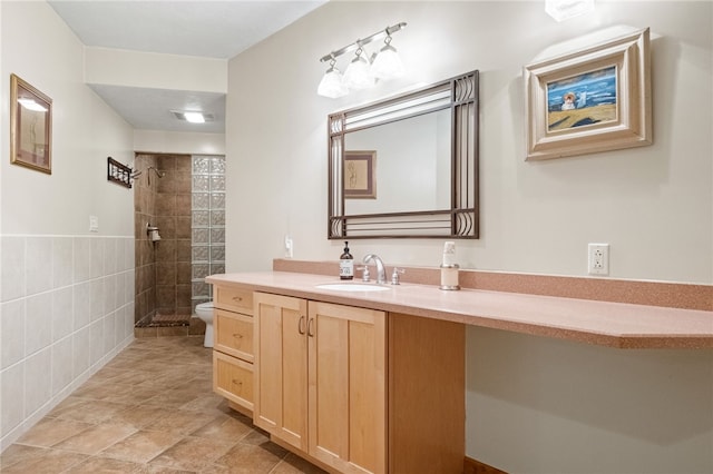 full bathroom with toilet, tile walls, tiled shower, and vanity