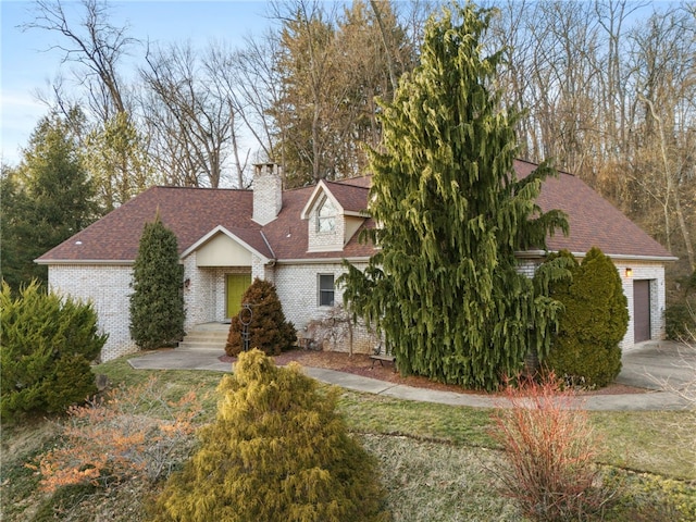 view of front of house featuring a shingled roof, a chimney, and brick siding