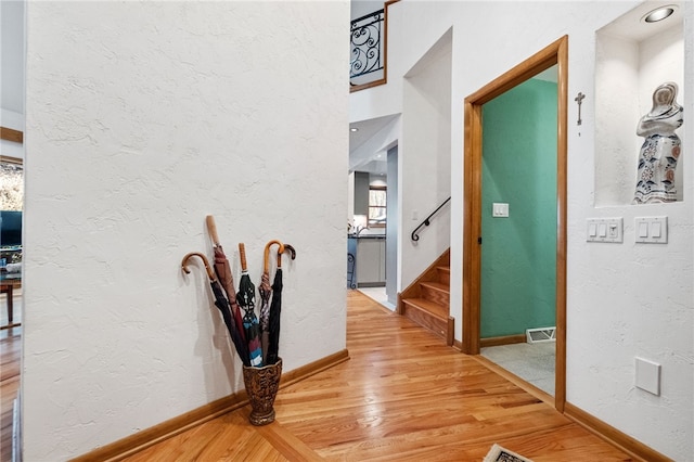 corridor featuring light wood-type flooring, stairs, visible vents, and a textured wall