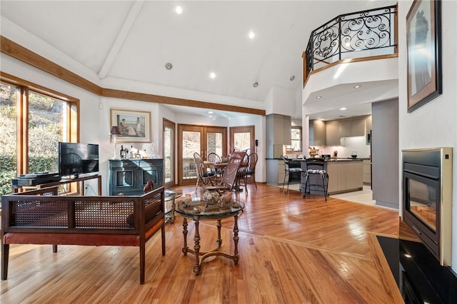 living area with high vaulted ceiling, a glass covered fireplace, plenty of natural light, and light wood finished floors