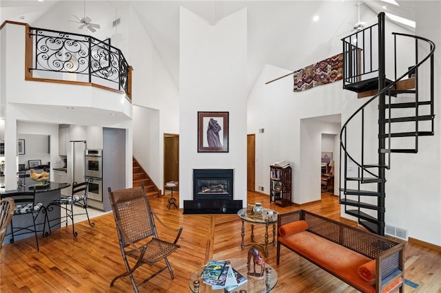 living room with ceiling fan, a high ceiling, wood finished floors, stairway, and a glass covered fireplace