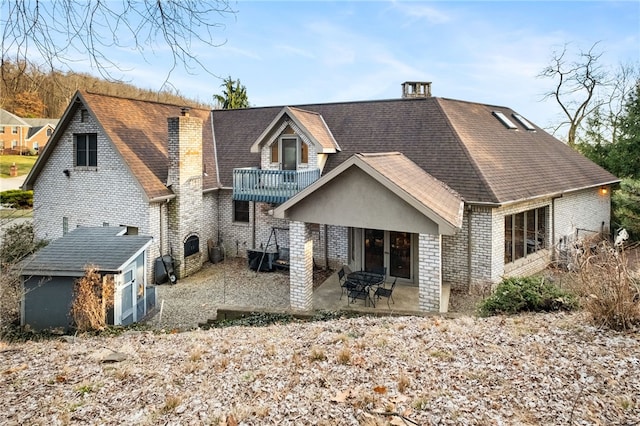 back of property with a patio, a balcony, brick siding, french doors, and roof with shingles