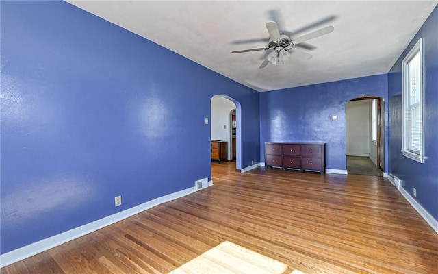 spare room with baseboards, visible vents, arched walkways, and wood finished floors