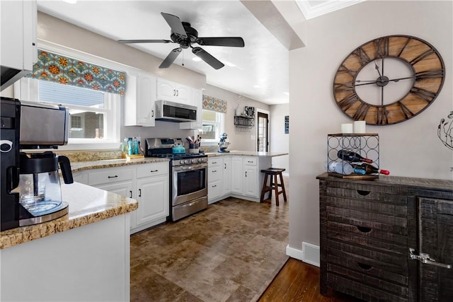 kitchen with a ceiling fan, appliances with stainless steel finishes, dark wood-type flooring, a peninsula, and white cabinetry