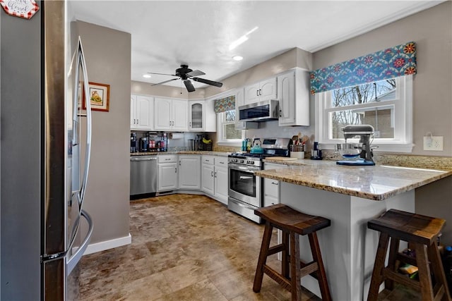 kitchen featuring white cabinets, appliances with stainless steel finishes, light stone counters, a peninsula, and a kitchen bar