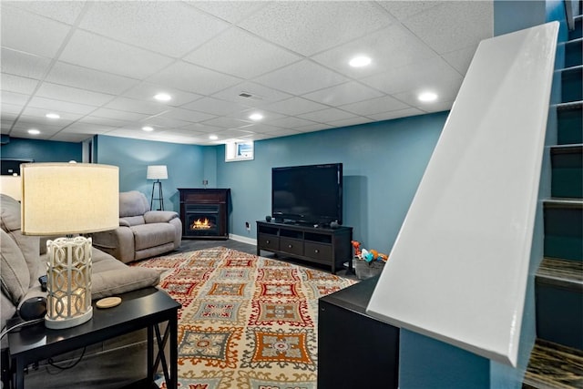 living room featuring a warm lit fireplace, visible vents, a drop ceiling, and recessed lighting