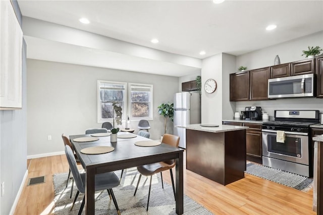 kitchen featuring stainless steel appliances, visible vents, light wood-style floors, a kitchen island, and dark brown cabinets