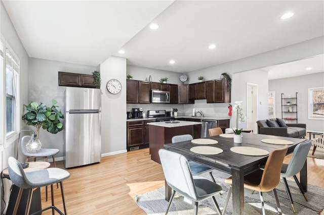 kitchen with light countertops, light wood-style flooring, appliances with stainless steel finishes, a kitchen island, and dark brown cabinets