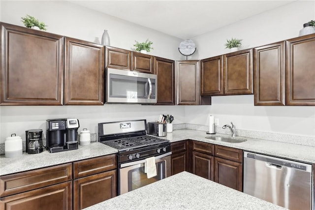 kitchen featuring stainless steel appliances, dark brown cabinets, a sink, and light stone countertops