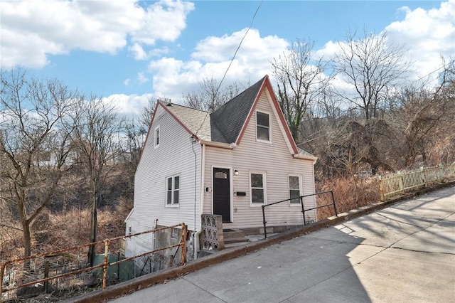 view of front facade with roof with shingles and fence