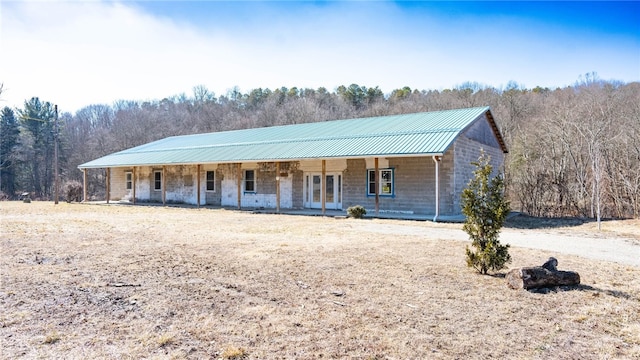 view of front facade featuring covered porch, stone siding, metal roof, and a view of trees