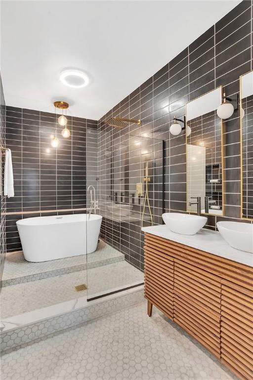 bathroom with a sink, double vanity, a freestanding tub, and tile walls