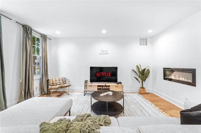 living room with wood finished floors, a glass covered fireplace, visible vents, and recessed lighting