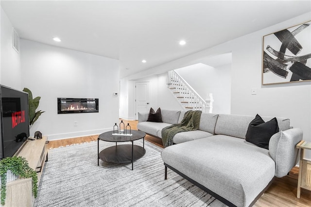 living room with recessed lighting, stairway, a glass covered fireplace, wood finished floors, and baseboards