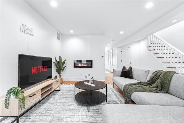 living room featuring recessed lighting, wood finished floors, visible vents, stairway, and a glass covered fireplace