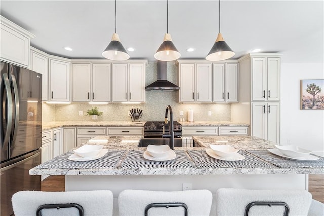 kitchen featuring hanging light fixtures, wall chimney range hood, freestanding refrigerator, light stone countertops, and tasteful backsplash