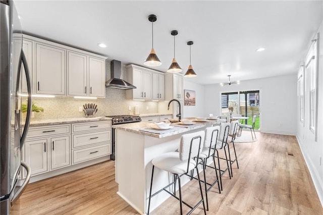 kitchen featuring stainless steel appliances, wall chimney range hood, light wood-type flooring, and tasteful backsplash