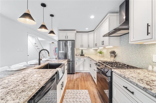 kitchen featuring stainless steel fridge with ice dispenser, black gas range oven, dishwashing machine, wall chimney exhaust hood, and white cabinetry