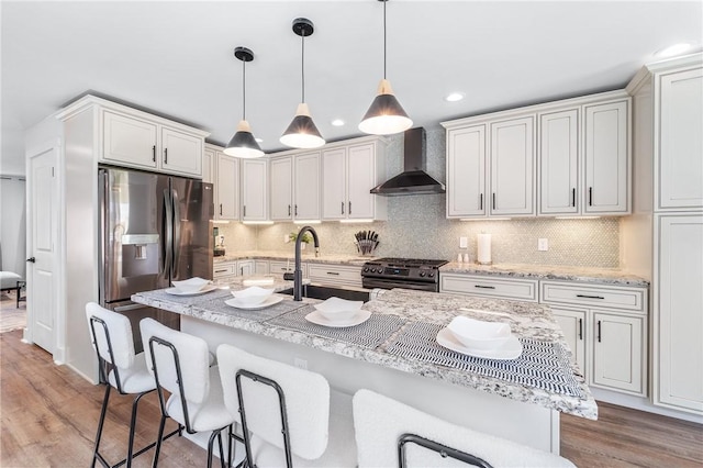 kitchen with a breakfast bar area, appliances with stainless steel finishes, light wood-type flooring, wall chimney range hood, and a sink