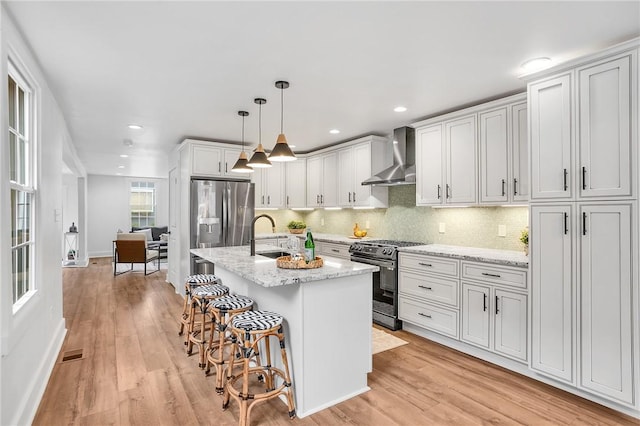 kitchen with light wood-type flooring, wall chimney exhaust hood, appliances with stainless steel finishes, and tasteful backsplash