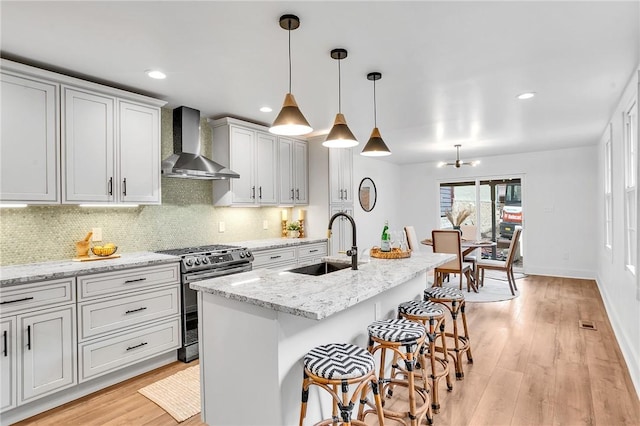 kitchen featuring a sink, light wood-type flooring, wall chimney exhaust hood, tasteful backsplash, and gas range