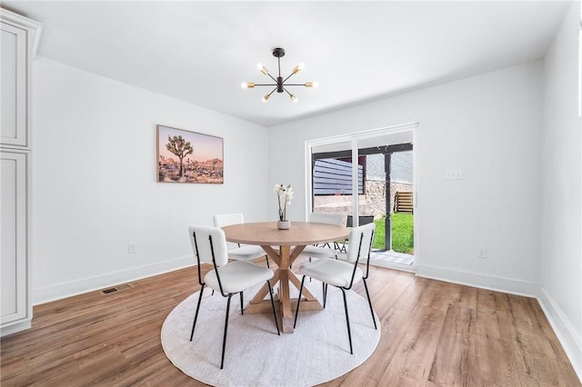 dining area featuring light wood-type flooring, visible vents, a notable chandelier, and baseboards