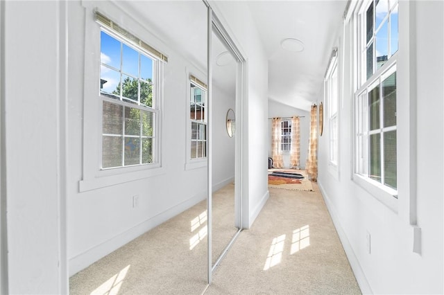 corridor with baseboards, lofted ceiling, and light colored carpet