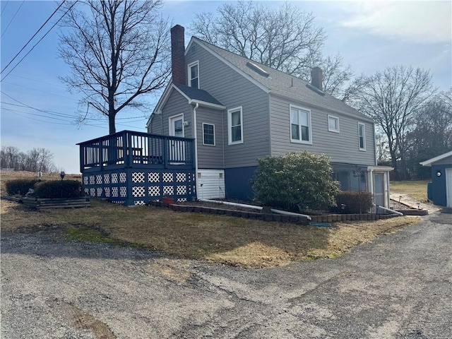 view of property exterior with a deck, roof with shingles, and a chimney