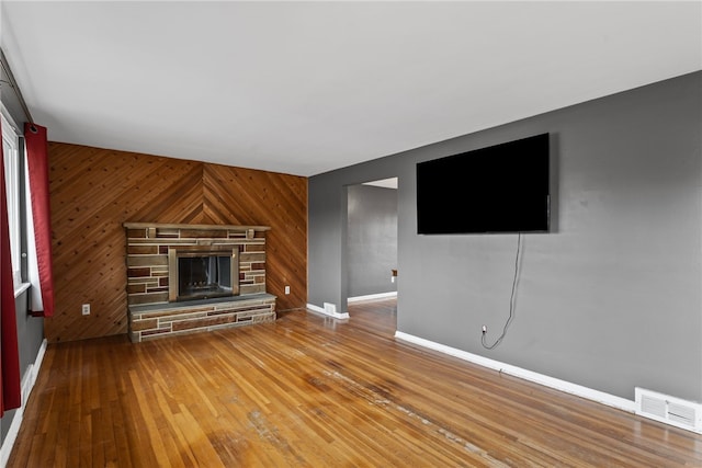 unfurnished living room with wooden walls, visible vents, baseboards, wood-type flooring, and a stone fireplace