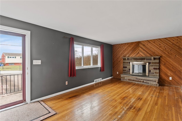 unfurnished living room with hardwood / wood-style flooring, wooden walls, a fireplace, visible vents, and baseboards