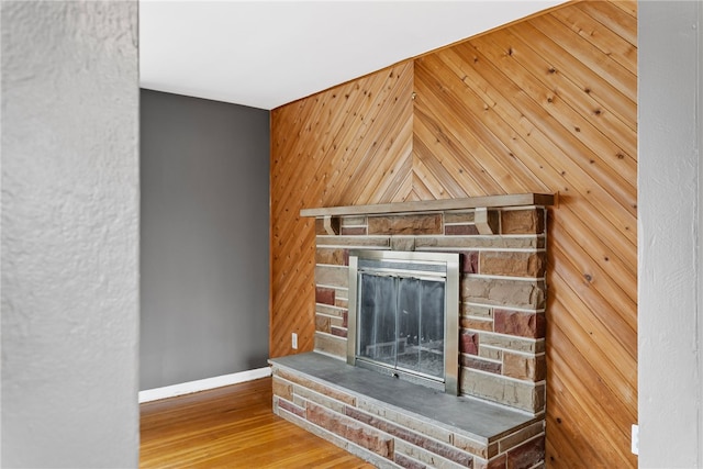 interior details with a fireplace, wood walls, baseboards, and wood finished floors