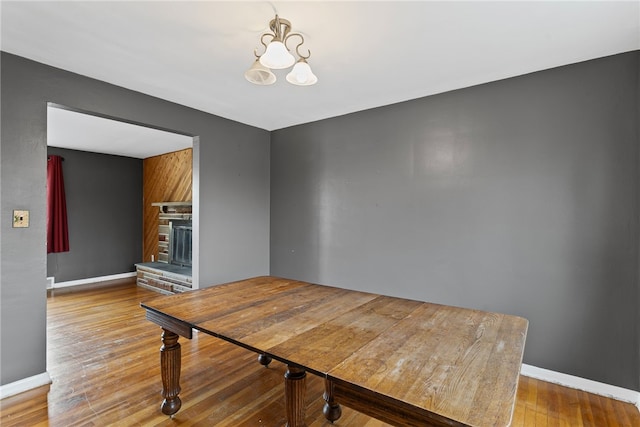 dining space featuring a fireplace with raised hearth, baseboards, wood finished floors, and a chandelier