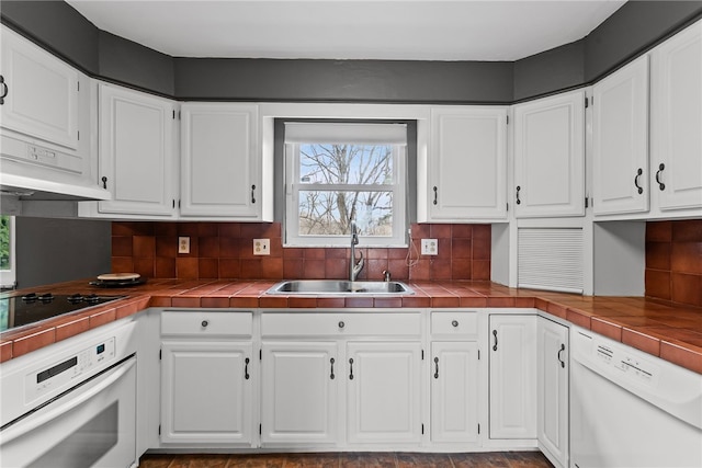 kitchen with tile counters, white appliances, white cabinetry, and a sink