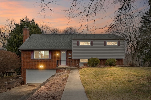 split level home with roof with shingles, a chimney, concrete driveway, an attached garage, and a front lawn