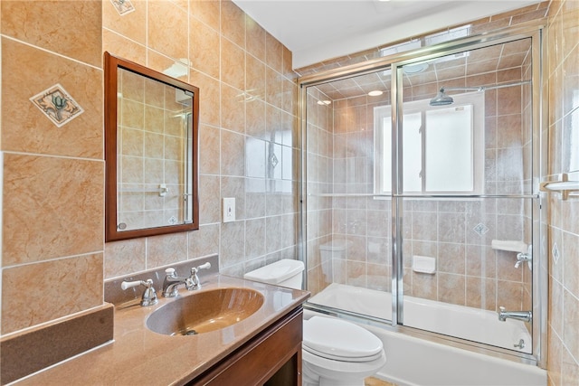 full bath featuring toilet, vanity, tile walls, combined bath / shower with glass door, and decorative backsplash