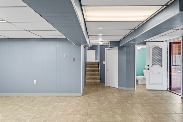 finished below grade area featuring a paneled ceiling, baseboards, and stairway