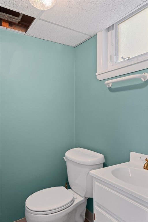 bathroom featuring a drop ceiling, vanity, toilet, and baseboards